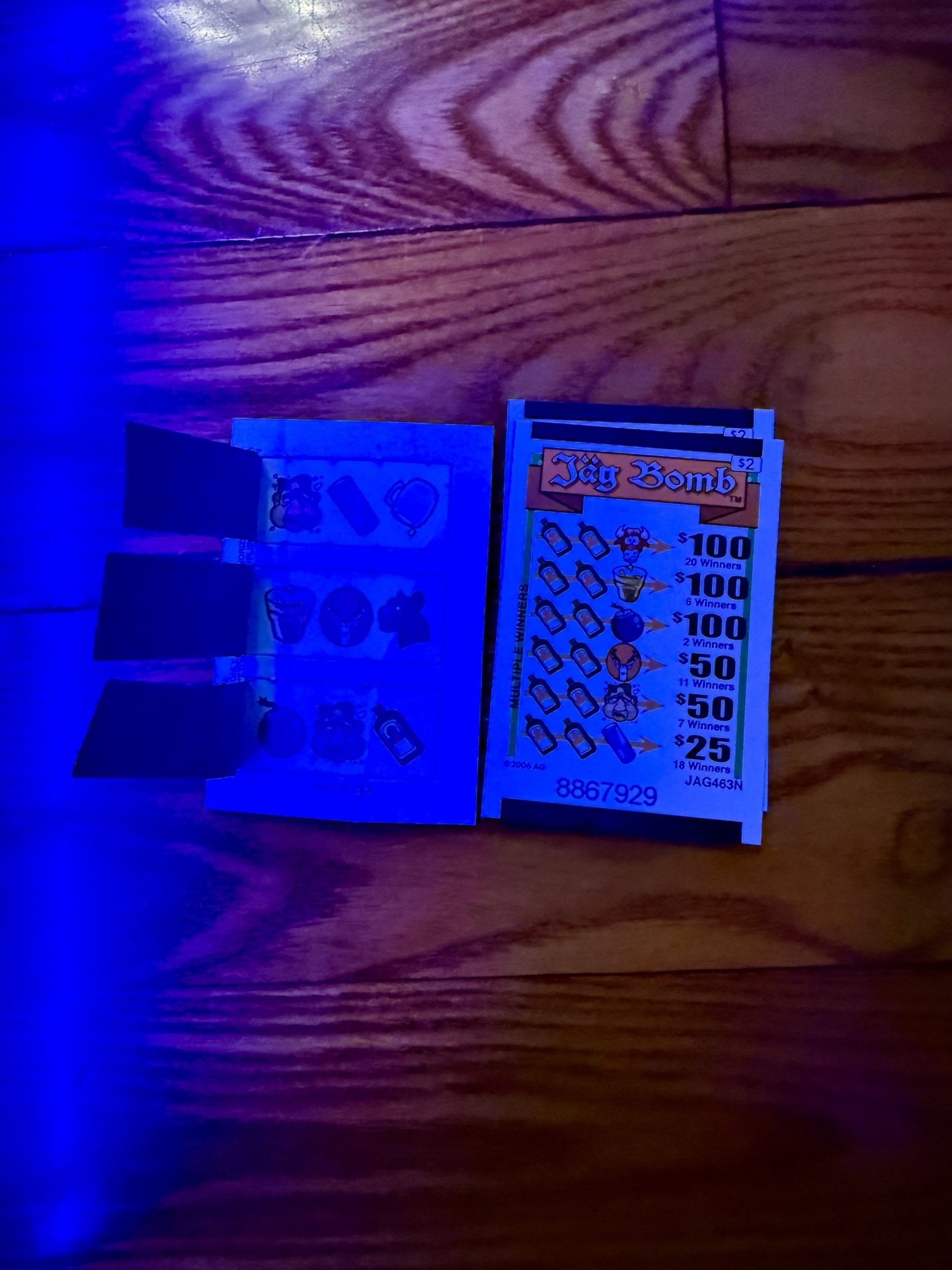 A pull-tab ticket with sections revealing jägermeister bottles and associated icons is placed on a wooden floor.