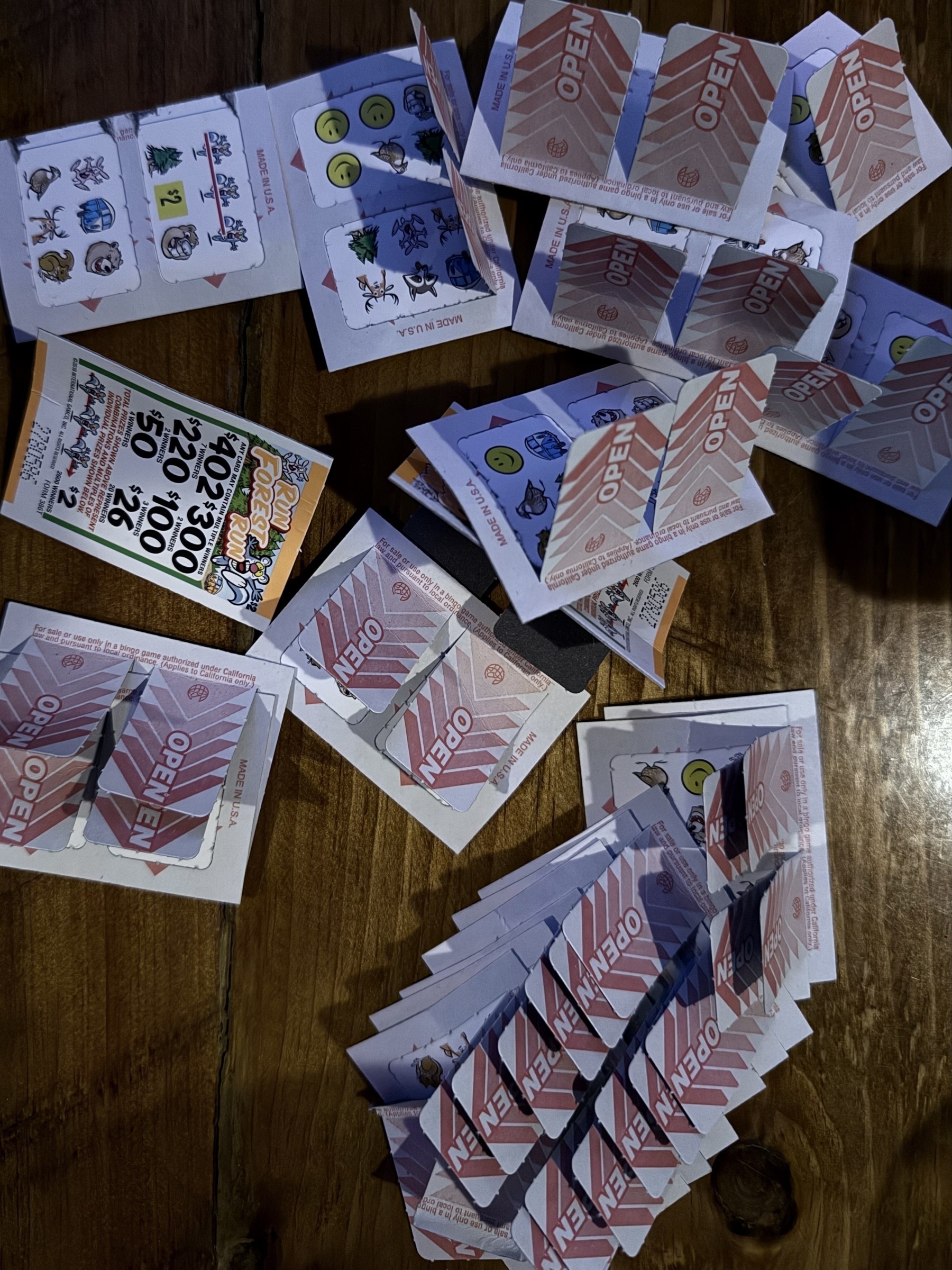 Auto-generated description: A collection of partially scratched lottery scratch-off tickets is scattered on a wooden surface.