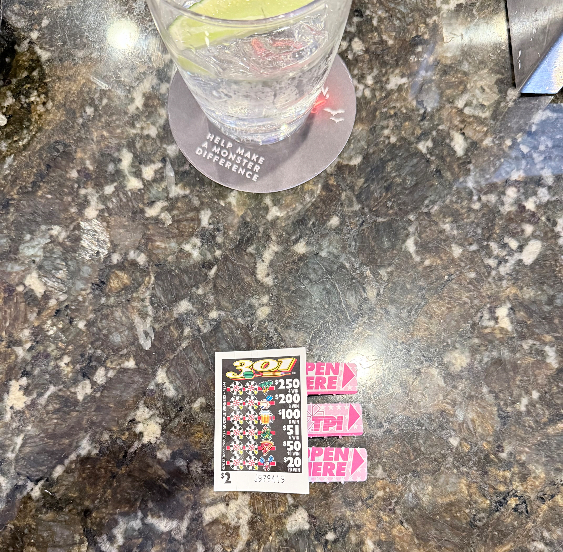 a pull-tab in the lower half of image on a dark marble table, with a clear cocktail and lime in the glass at the upper half of the image